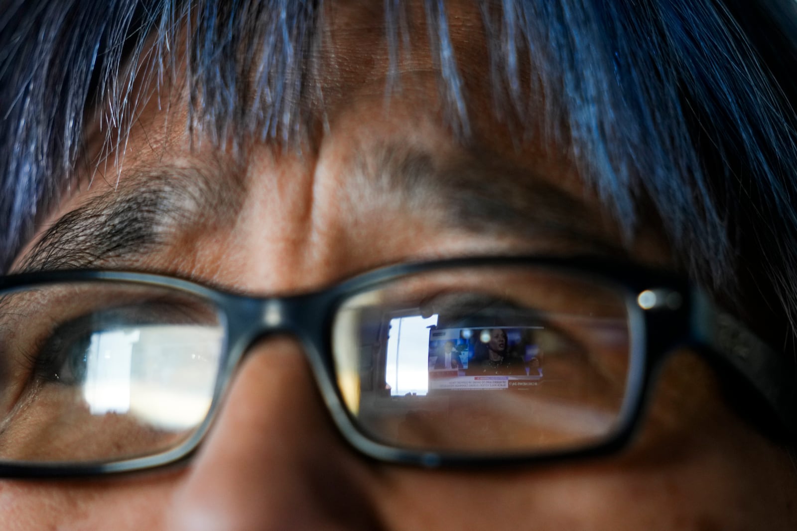 A CBS News broadcast showing Democratic presidential nominee Vice President Kamala Harris is reflected in the eyeglasses of Alice Aishanna as she watches television at her home in Kaktovik, Alaska, Tuesday, Oct. 15, 2024. (AP Photo/Lindsey Wasson)