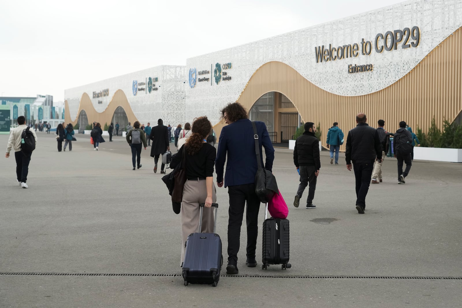 Attendees pull luggage as they walk into the venue for the COP29 U.N. Climate Summit, Saturday, Nov. 23, 2024, in Baku, Azerbaijan. (AP Photo/Sergei Grits)