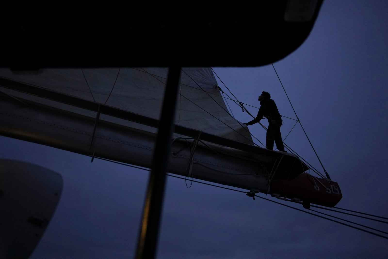 A sailor stands on the boom to check the folding of the mainsail of the sailboat ''Grain de Sail II' as it sails off Saint Malo, western France, Nov. 6, 2024. (AP Photo/Thibault Camus)