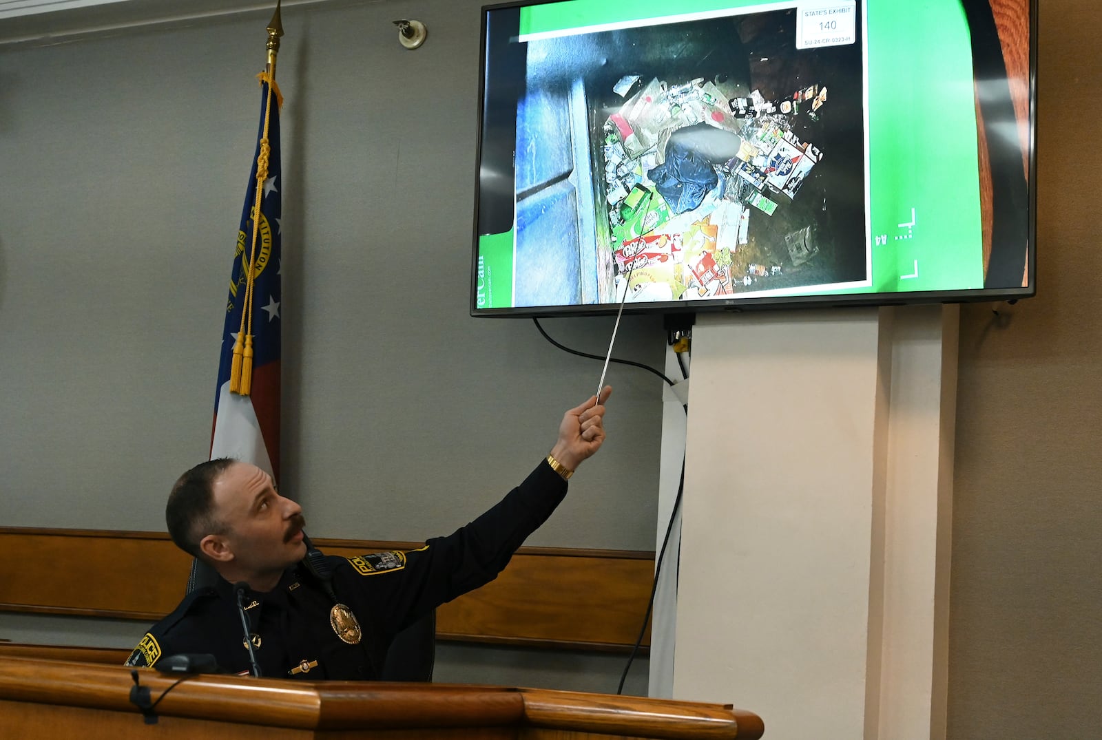 Athens-Clarke County police officer Zachary Davis points out the jacket he collected from a dumpster on photograph as he testifies on the witness stand during a trial of Jose Ibarra, accused of killing a Georgia nursing student earlier this year, at Athens-Clarke County Superior Court, Friday, Nov. 15, 2024, in Athens, Ga. (Hyosub Shin/Atlanta Journal-Constitution via AP, Pool)