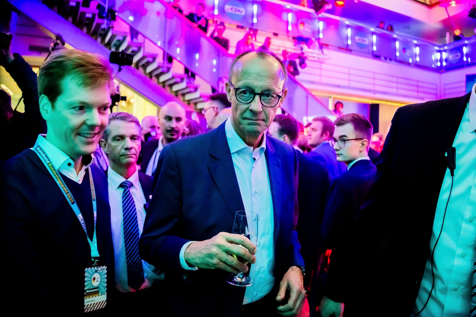 Friedrich Merz, center, leader of the Christian Democratic Union (CDU), walks in the Konrad Adenauer House with a glass of beer in his hand in Berlin, Sunday, Feb. 23, 2025. (Christoph Soeder/dpa via AP)