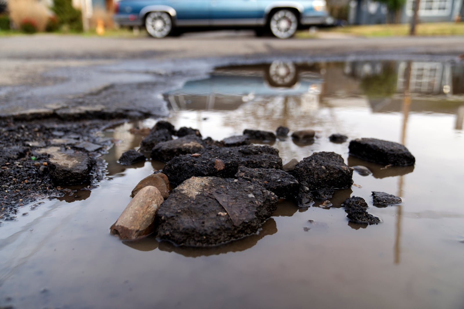 A car drives by a pot hole filled with rain water on Thursday, Feb. 6, 2025, in Portland, Ore. (AP Photo/Jenny Kane)