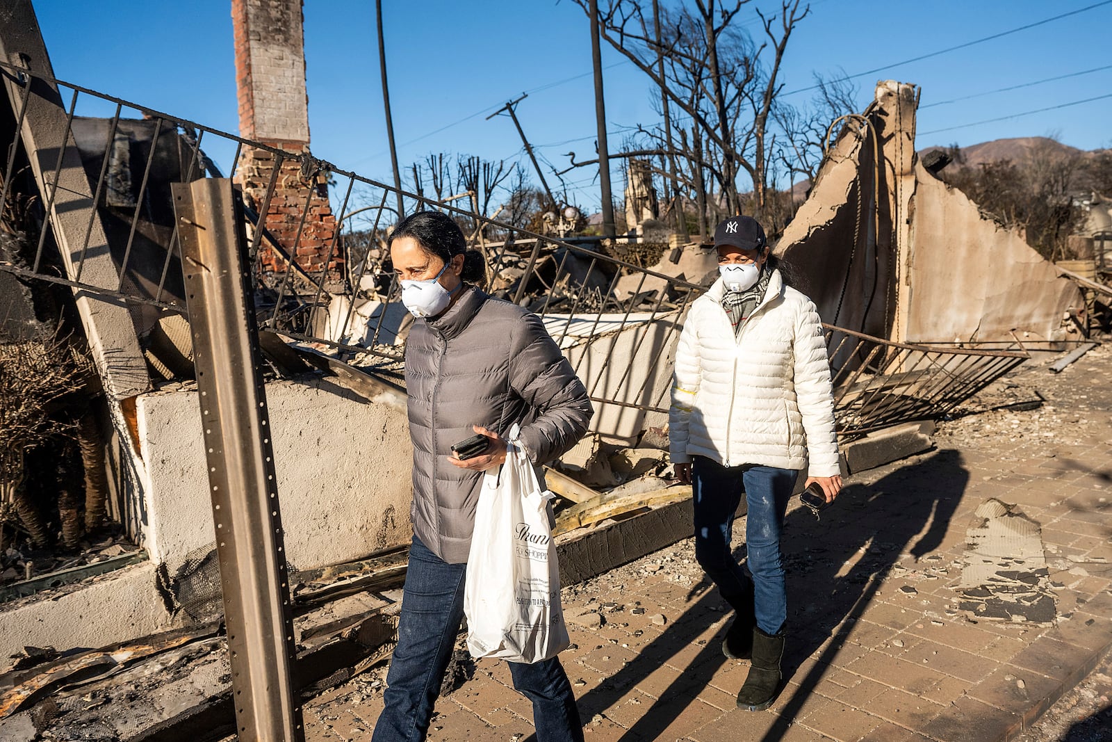 Marjan Rajabi carries items salvaged from her Pacific Palisades home, which was destroyed by the Palisades Fire, on Sunday, Jan. 12, 2025, in Los Angeles. Accompanying her is her sister Mitre Rajabi. (AP Photo/Noah Berger)