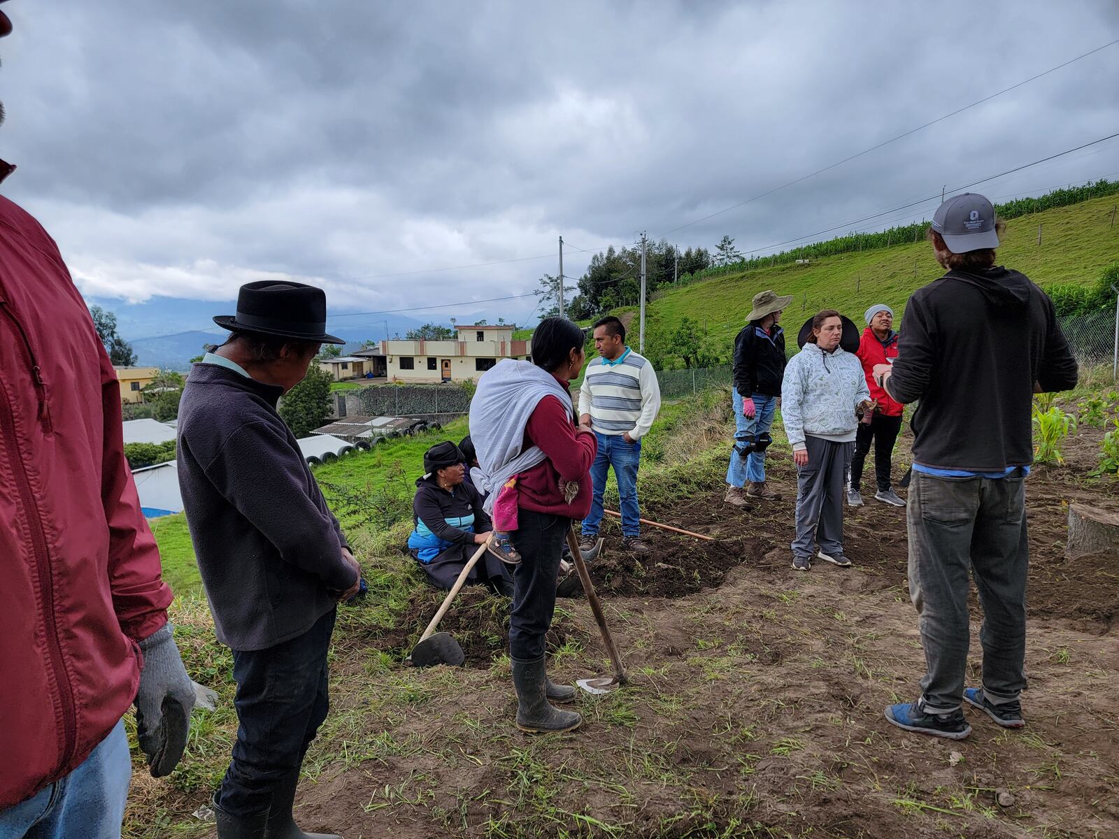 Waiting on instructions prior to planting; the lady in the red shirt with the white cloth on her back is carrying her baby while she works.