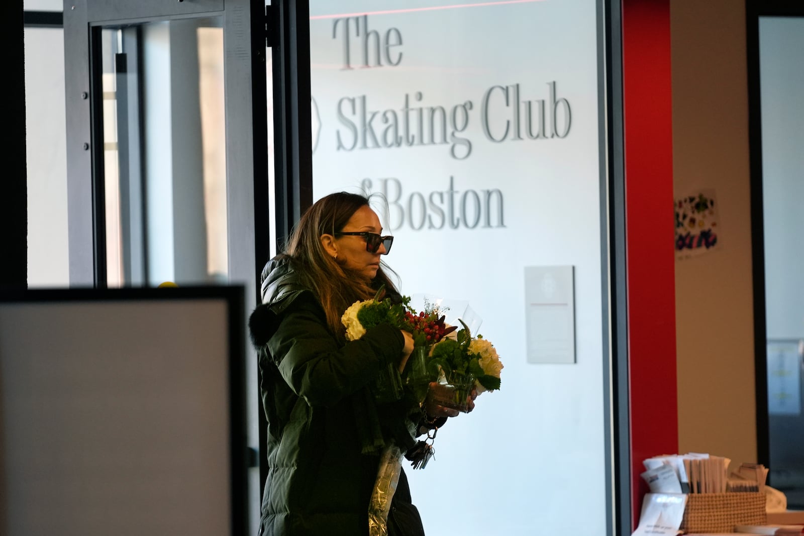 A woman brings flowers to The Skating Club of Boston, where six athletes, coaches and family associated with the club are believed to have perished in the collision of a passenger aircraft and military helicopter in Washington, Thursday, Jan. 30, 2025, in Norwood, Mass. (AP Photo/Robert F. Bukaty)