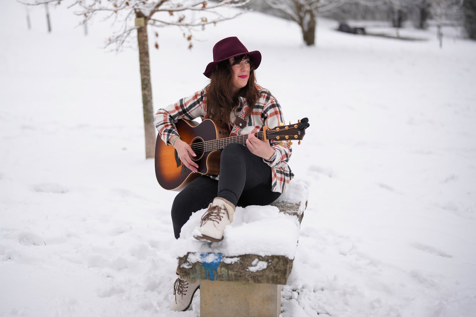 Victoria Collings plays her guitar as she sits on a bench in the snow Saturday, Jan. 11, 2025, in Nashville, Tenn. (AP Photo/George Walker IV)