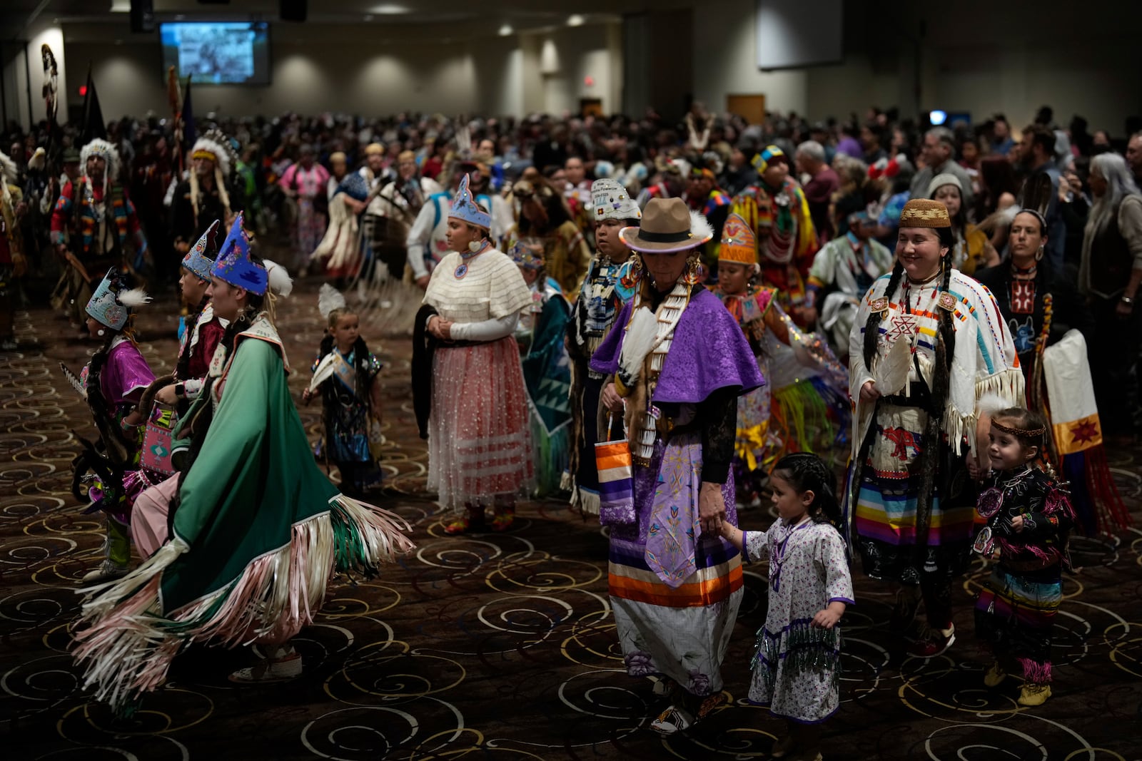 Tiffany Stuart, at right in white, holds hands with her daughter Kwestaani Chuski Stuart, bottom right, as they participate in a powwow at Chinook Winds Casino Resort, Saturday, Nov. 16, 2024, in Lincoln City, Ore. (AP Photo/Jenny Kane)