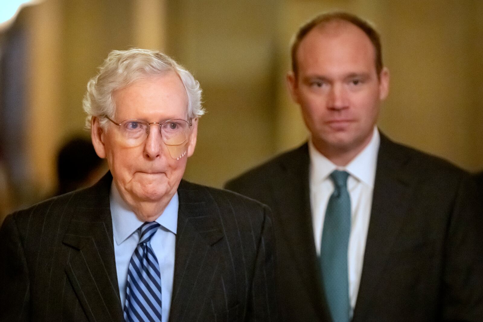 Senate Minority Leader Mitch McConnell of Ky., left, wears a bandage on his face as he walks to cast a vote on the Senate floor after falling during a luncheon on Capitol Hill, Tuesday, Dec. 10, 2024, in Washington. (AP Photo/Mark Schiefelbein)