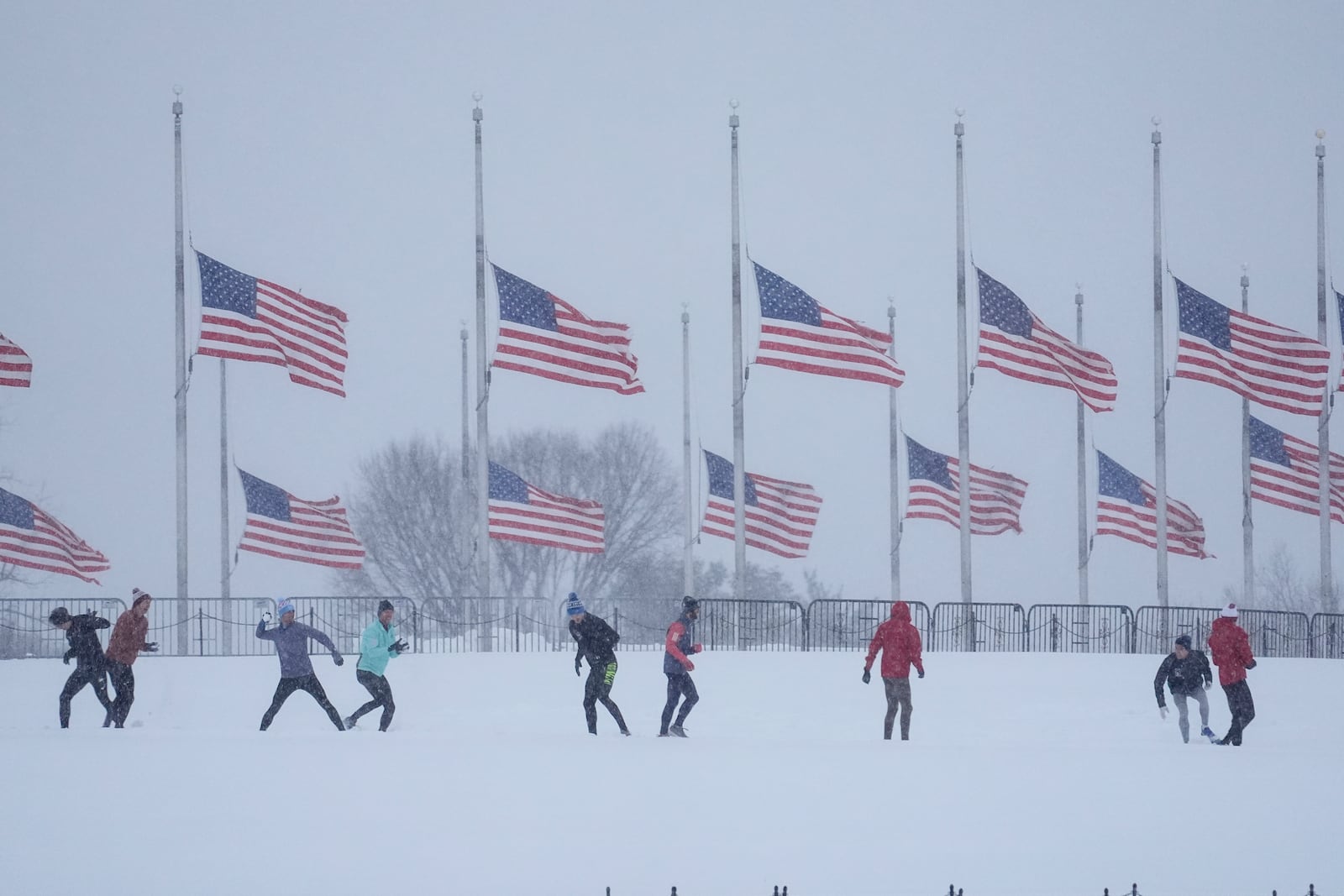 People engage in a snowball fight as U.S. flags, along the base of the Washington Monument, fly at half-staff in memorial to former President Jimmy Carter, who died at the age of 100, in Washington, Monday, Jan. 6, 2025. (AP Photo/Matt Rourke)