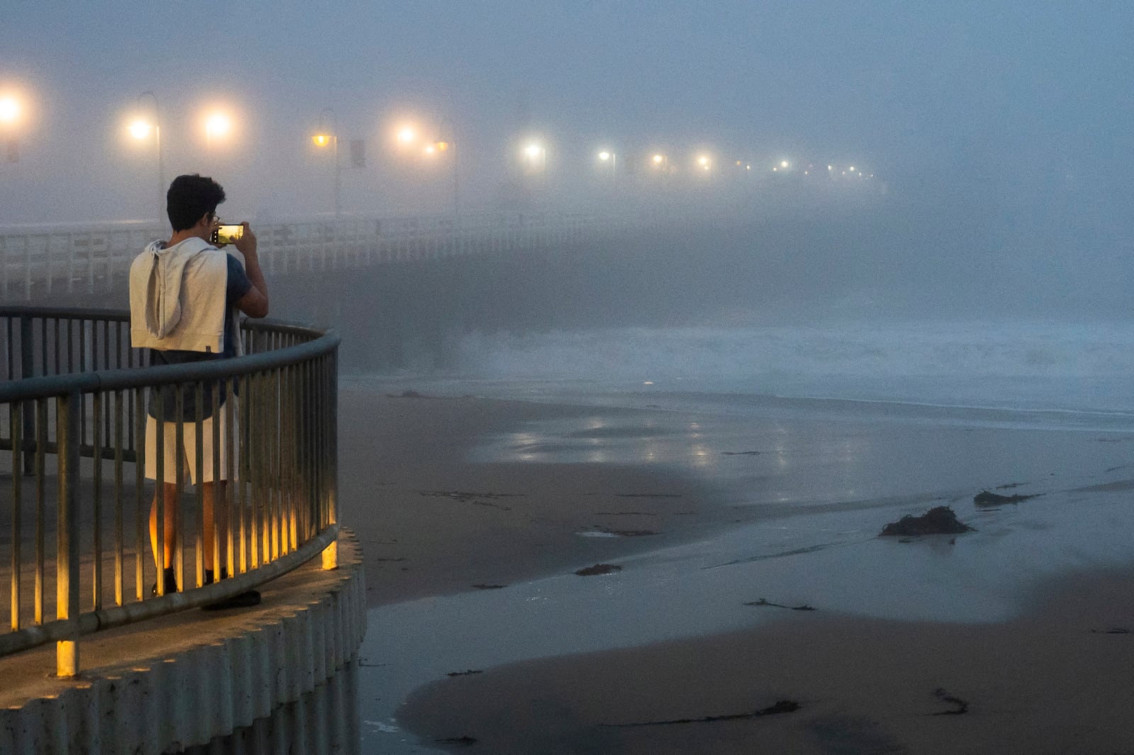 A person takes a photo of high surf near the Santa Cruz Wharf in Santa Cruz, Calif., Monday, Dec. 23, 2024. (AP Photo/Nic Coury)