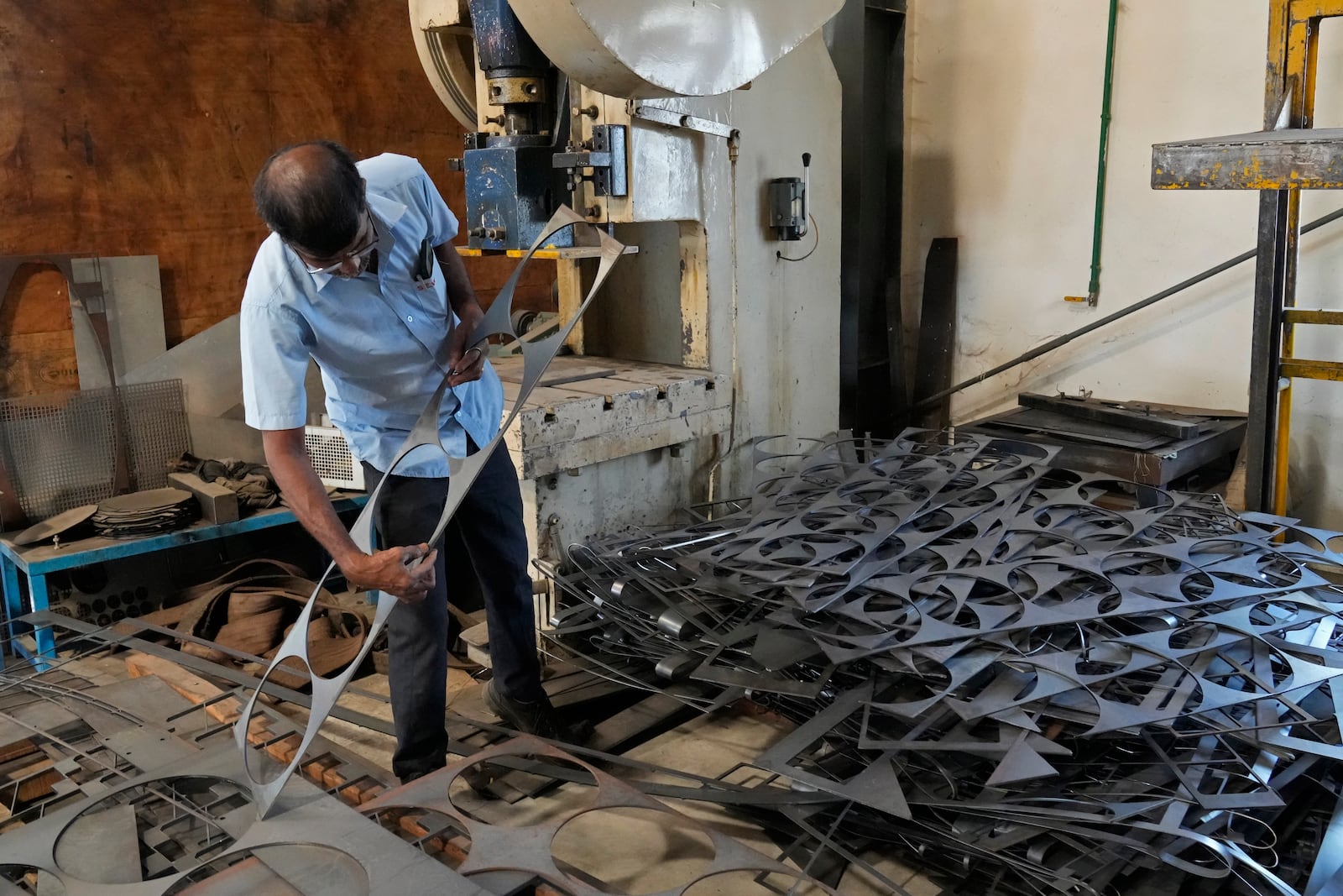 A worker looks for usable material from a pile of leftover steel sheets at a factory in a suburb of Bengaluru, India, Thursday, Feb. 27, 2025. (AP Photo/Aijaz Rahi)