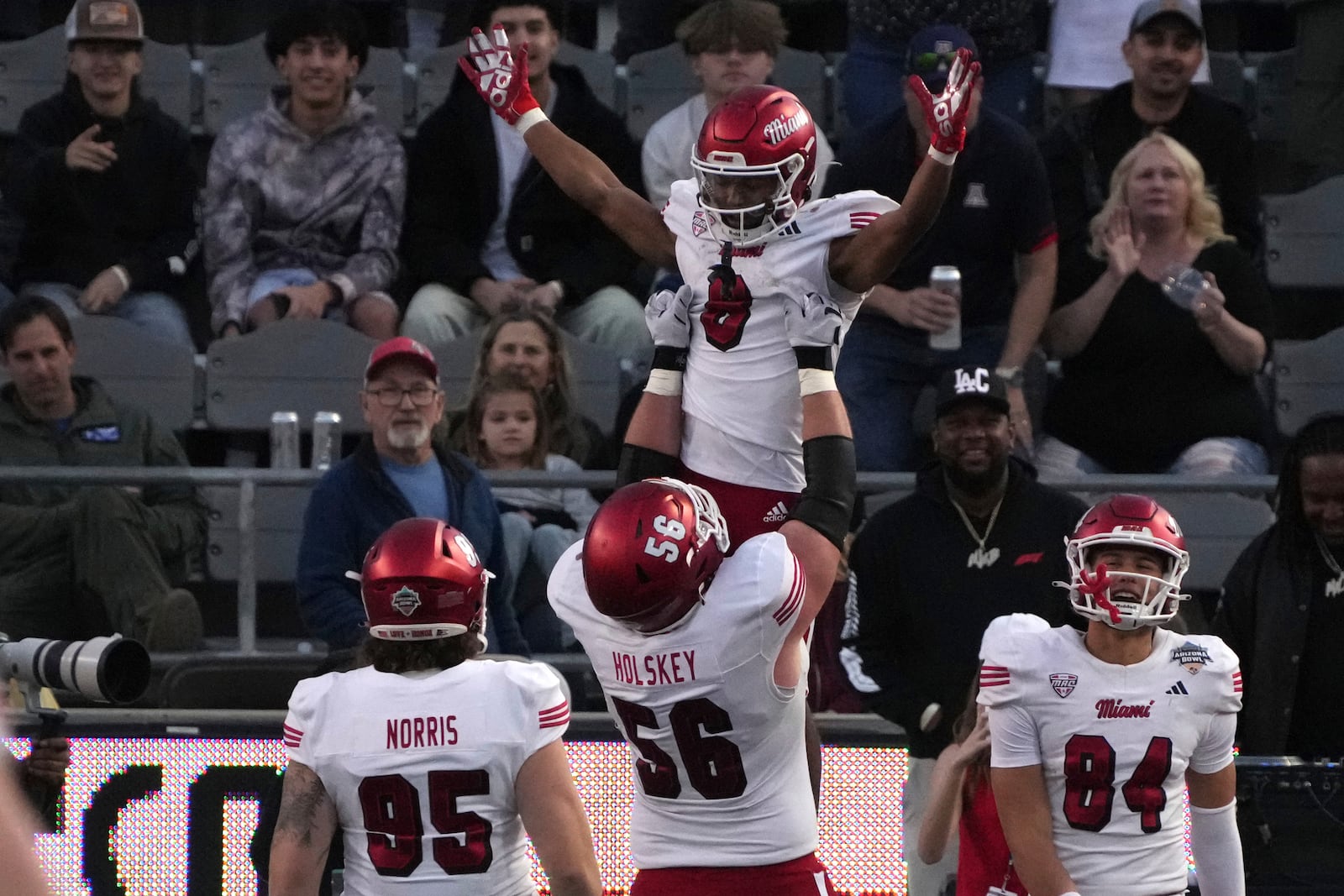 Miami (Ohio) running back Kevin Davis (8) is lifted by offensive lineman Reid Holskey (56) after scoring a touchdown against Colorado State in the second half of the Arizona Bowl NCAA college football game, Saturday, Dec. 28, 2024, in Tucson, Ariz. (AP Photo/Rick Scuteri)