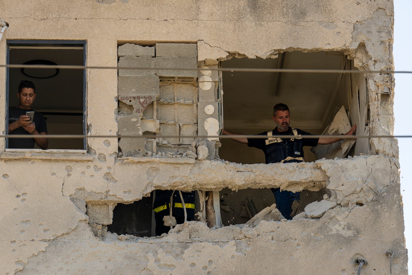 Municipality workers survey the damage to an apartment building struck by a rocket fired from Lebanon, in Kiryat Ata, northern Israel, Saturday, Oct. 19, 2024. (AP Photo/Ariel Schalit)