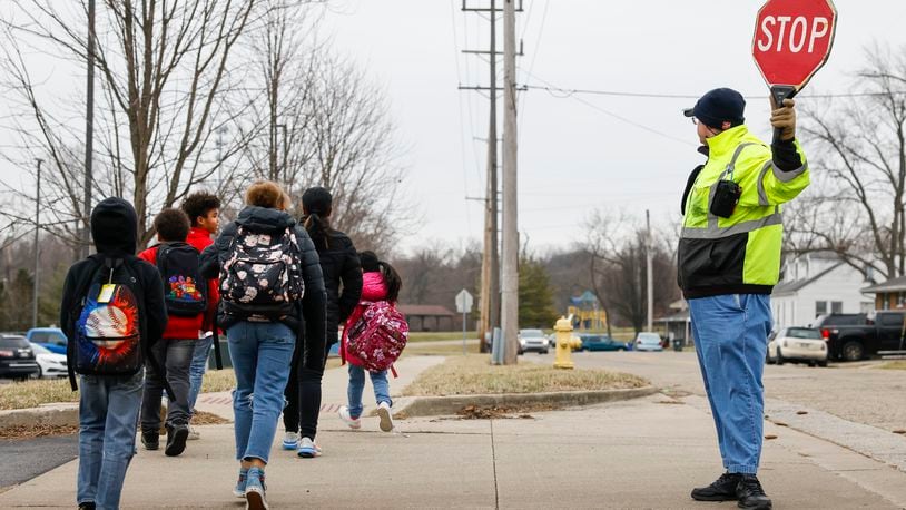 Crossing guard Donald Bushey helps students and parents cross the street as school lets out at Crawford Woods Elementary Friday, Feb. 10. 2023. The city on Hamilton will seek a grant from ODOT's Safe Routes to School Grant Program for infilling sidewalks and installing ADA compliant curb ramps, crosswalks, and signage around Crawford Woods Elementary School. NICK GRAHAM/STAFF